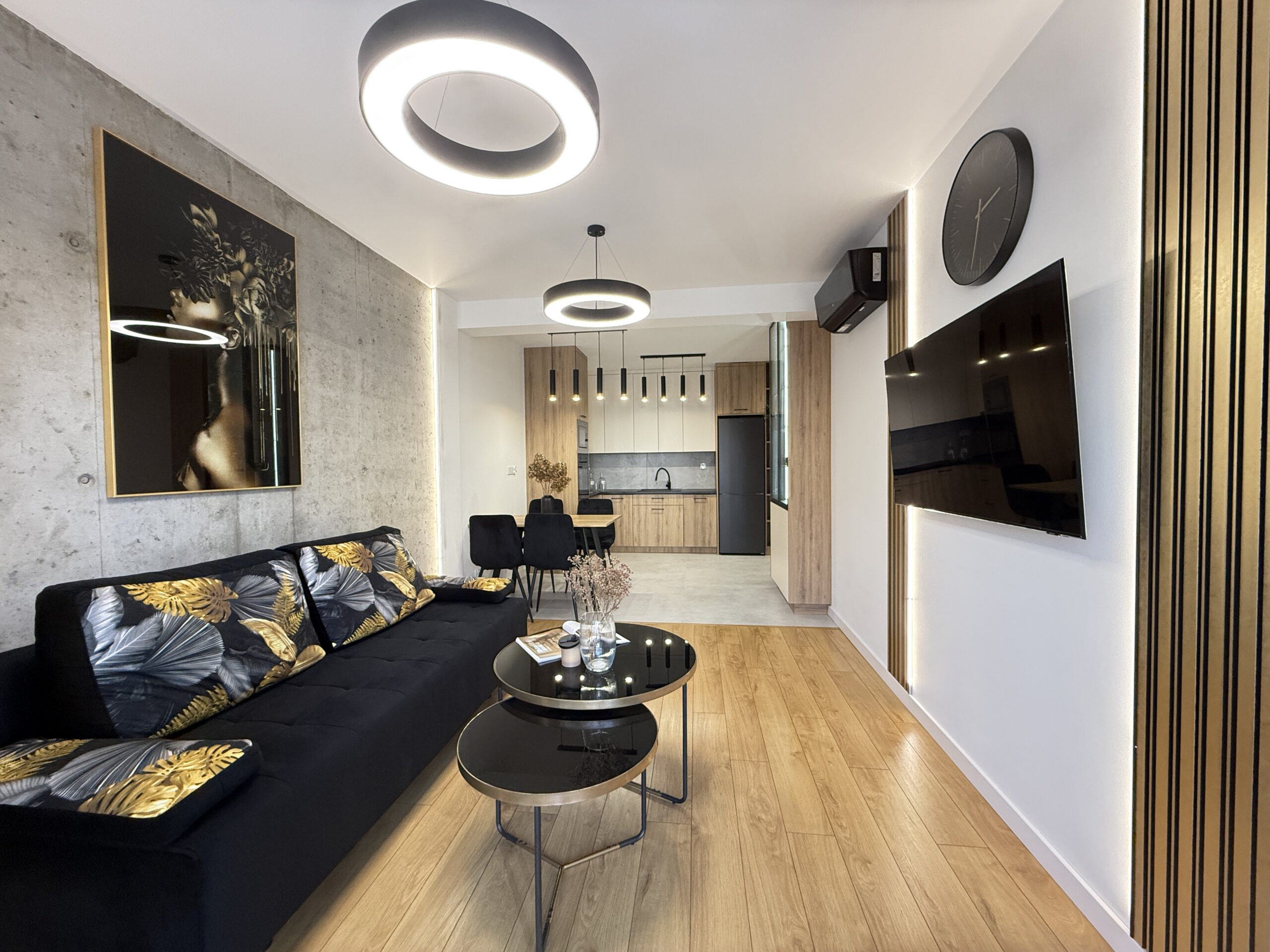 salon z aneksem kuchennym nowoczesny design czarny złoto lamele scenka tv szklany stolik